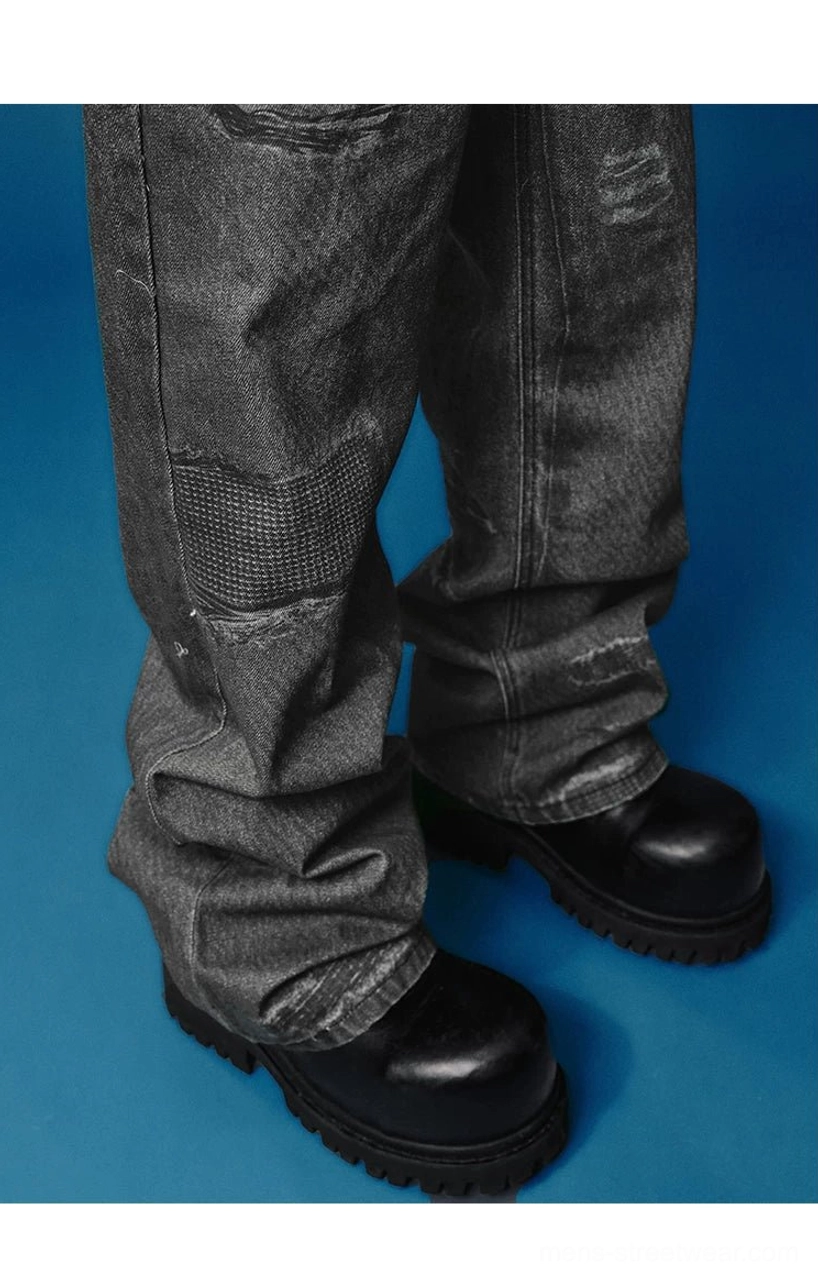 Low-angle close-up of black distressed wide-leg jeans showing frayed hems, repaired patches, vintage wash texture, and leather boots