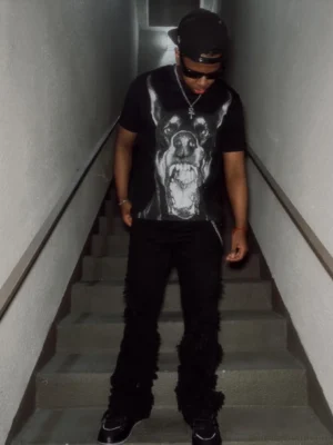 Male model styling black Doberman graphic streetwear T-shirt with flared pants cap sunglasses and silver necklace
