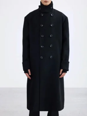 Black double-breasted long overcoat front close-up showing high collar button fastening wide cuffs and tailored streetwear construction
