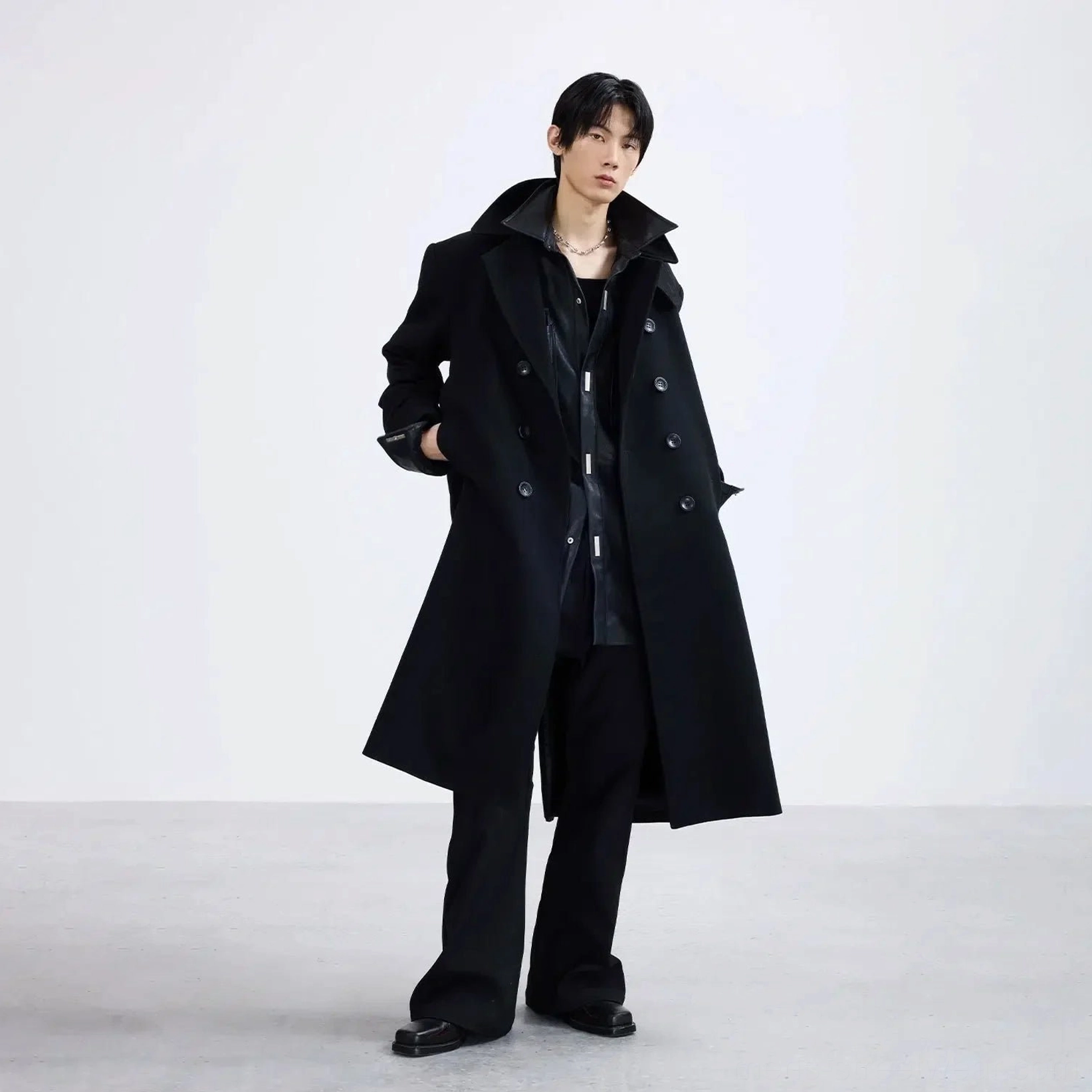 Male model wearing black double-breasted trench style long overcoat with notched lapel in Korean streetwear outfit