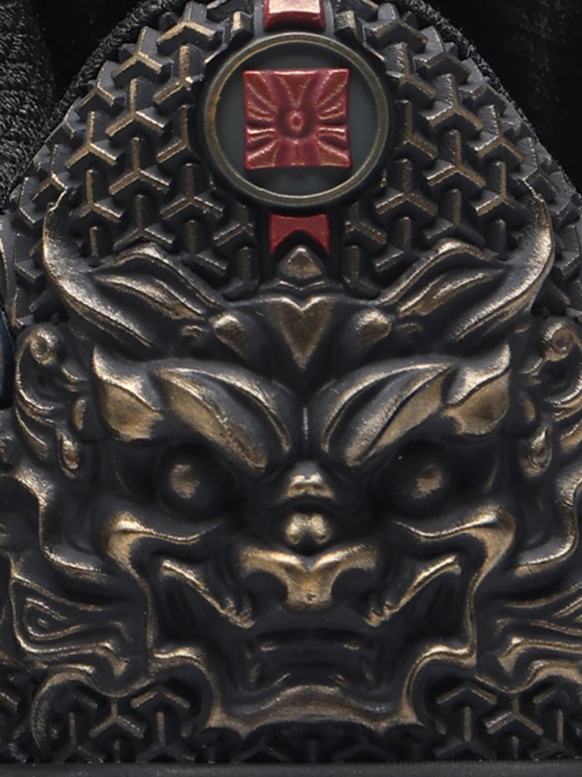 Close-up of bronze carved mythical face ornament with red square emblem on black dragon embroidered sneaker heel