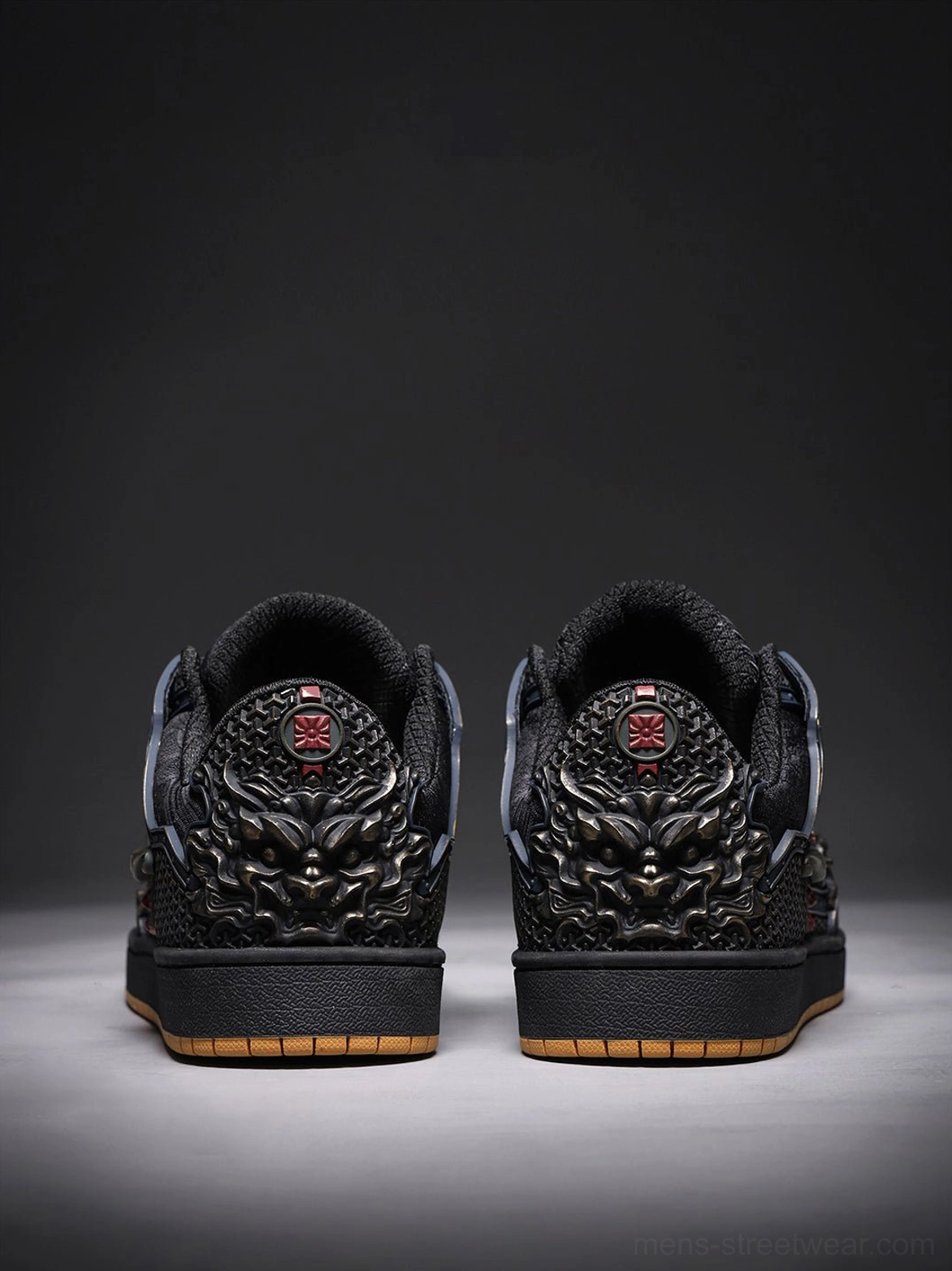 Rear view of black dragon sneakers showing bronze mythical face heel ornaments, red emblems, and gum rubber soles