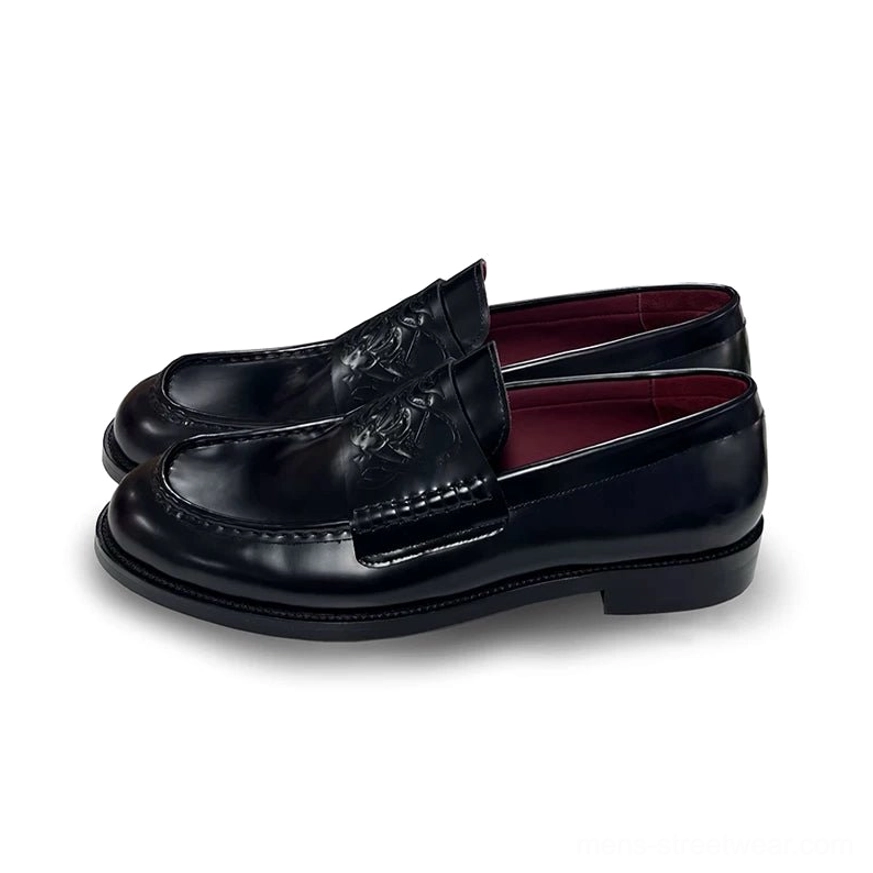 Black leather loafers shown in three-quarter view with embossed vamp detail, polished finish, neat stitching, and deep burgundy interior