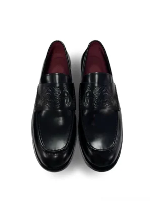 Black embossed leather loafers shown from a top-down view with glossy square toes, decorative vamp texture, and burgundy lambskin lining