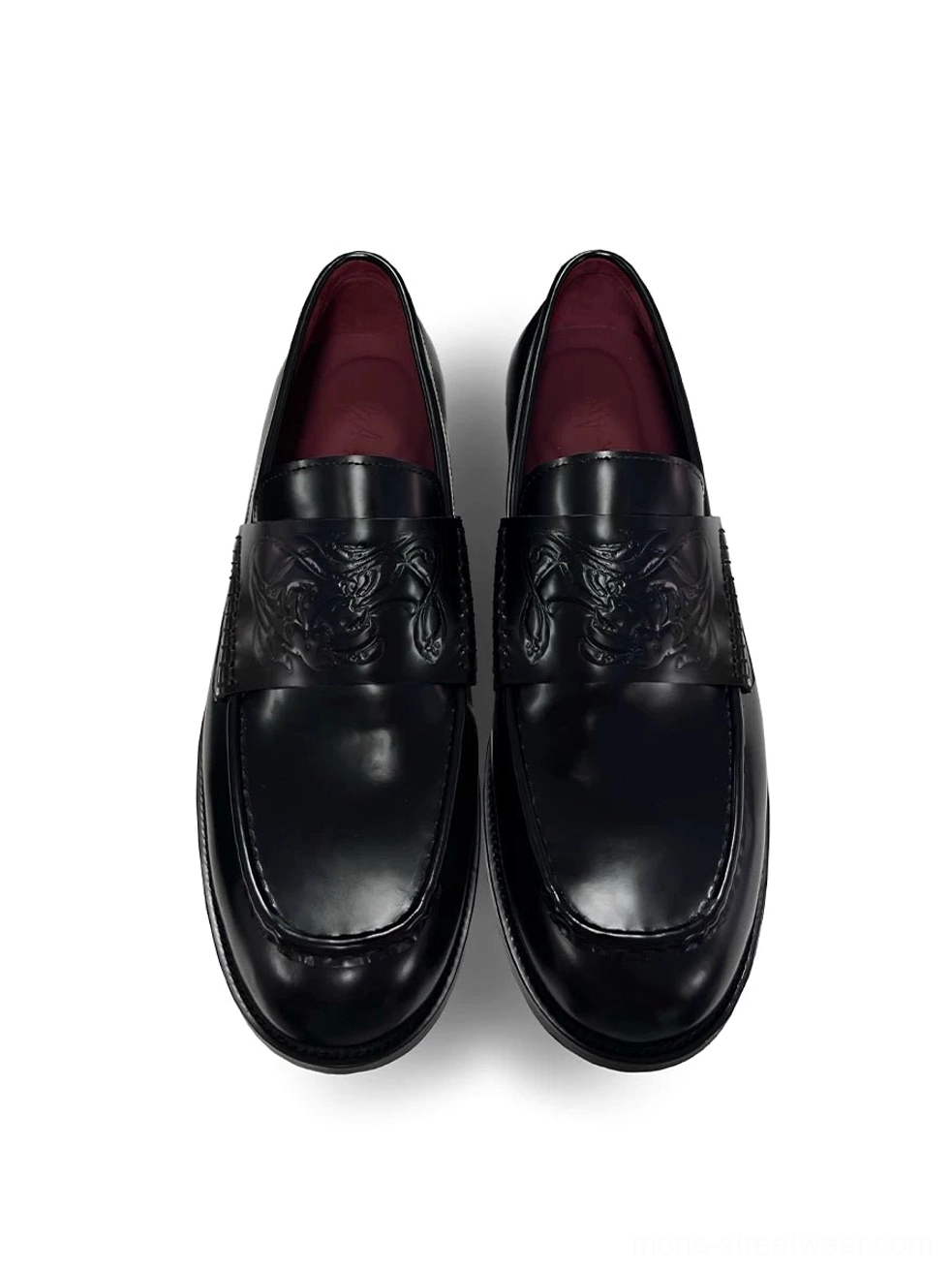 Black embossed leather loafers shown from a top-down view with glossy square toes, decorative vamp texture, and burgundy lambskin lining