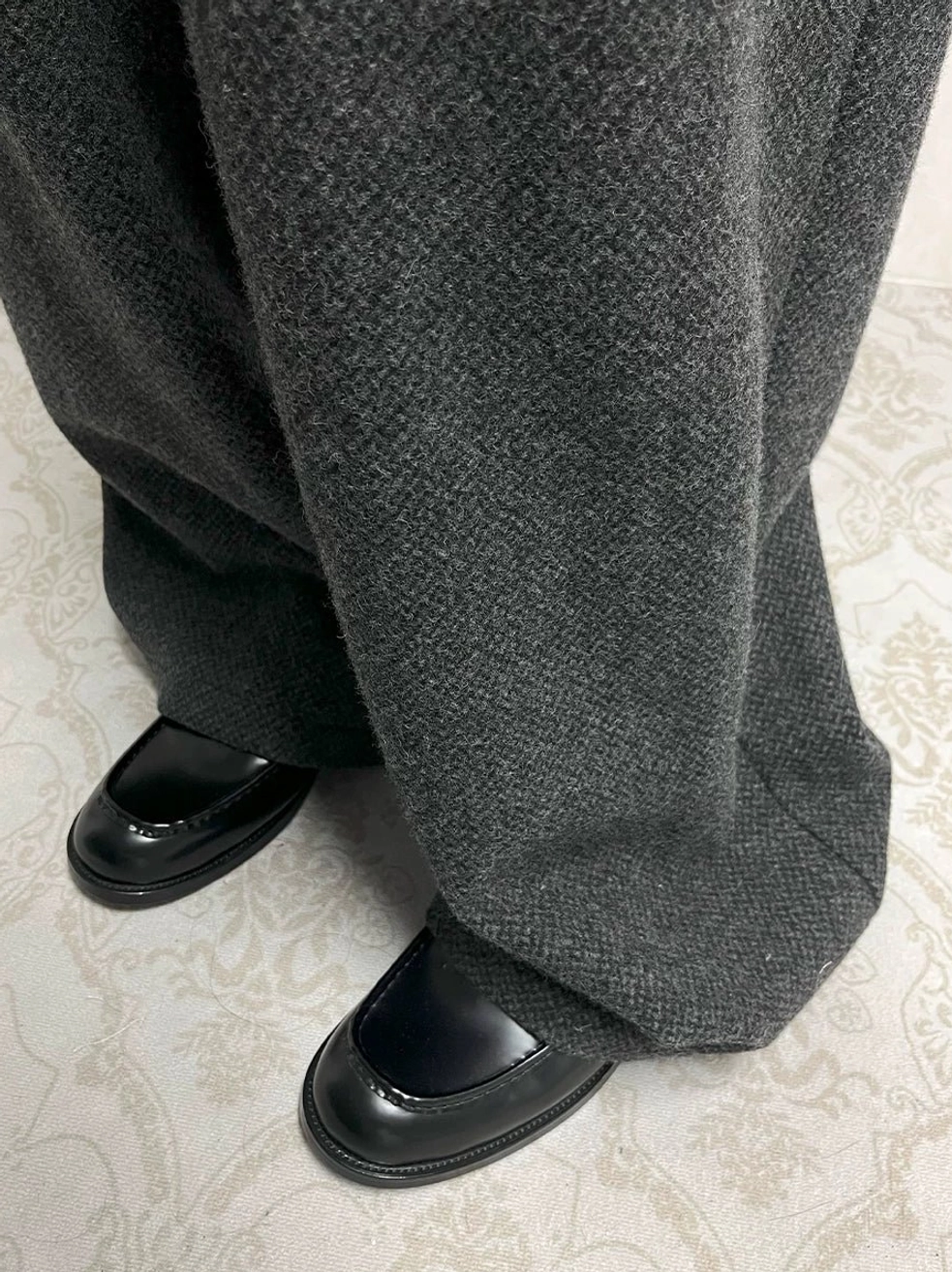 Black embossed leather loafers paired with grey wide-leg trousers in a contemporary smart casual streetwear outfit