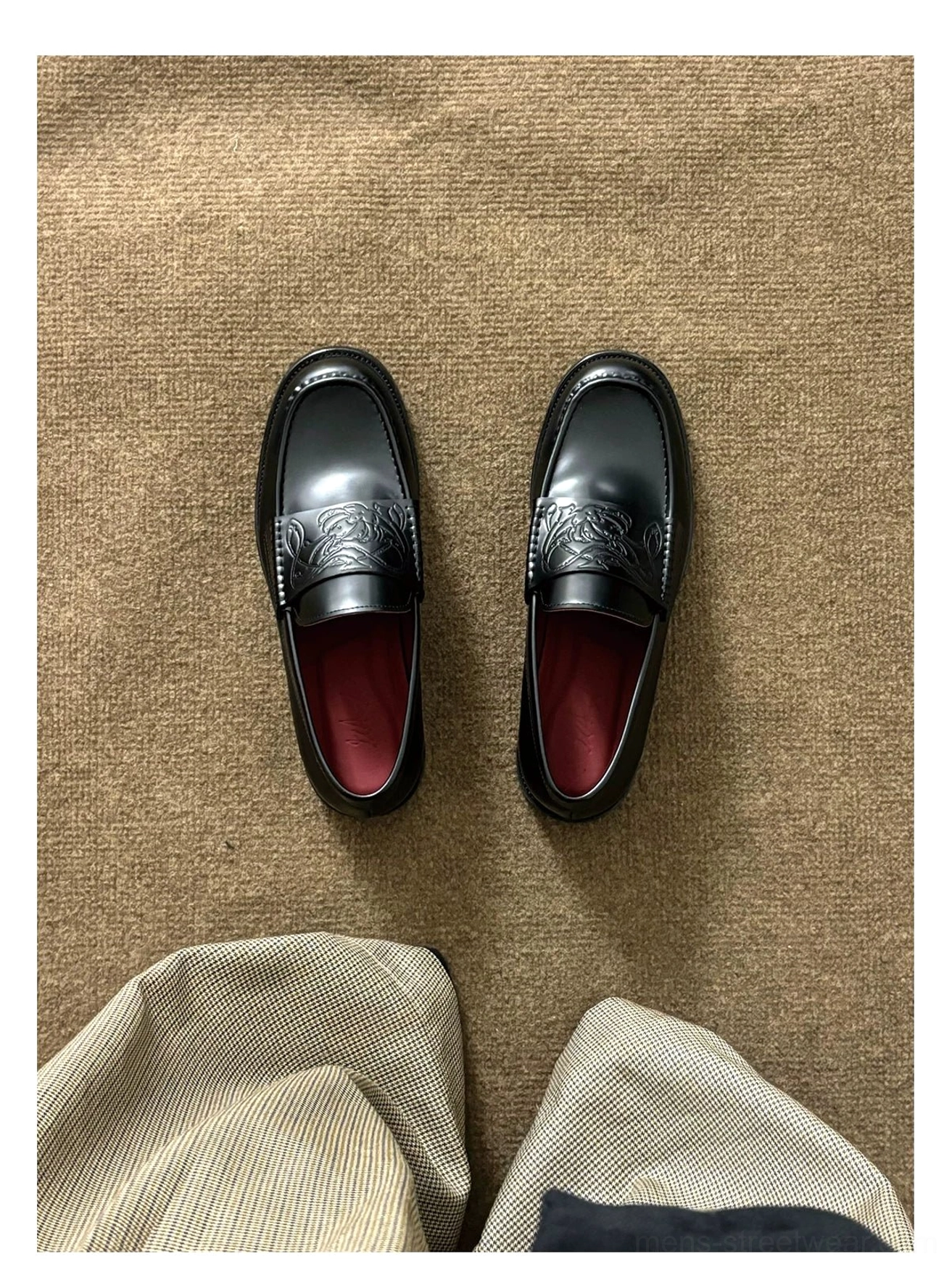 Black embossed leather loafers arranged with tailored trousers on textured brown fabric for a refined contemporary streetwear look