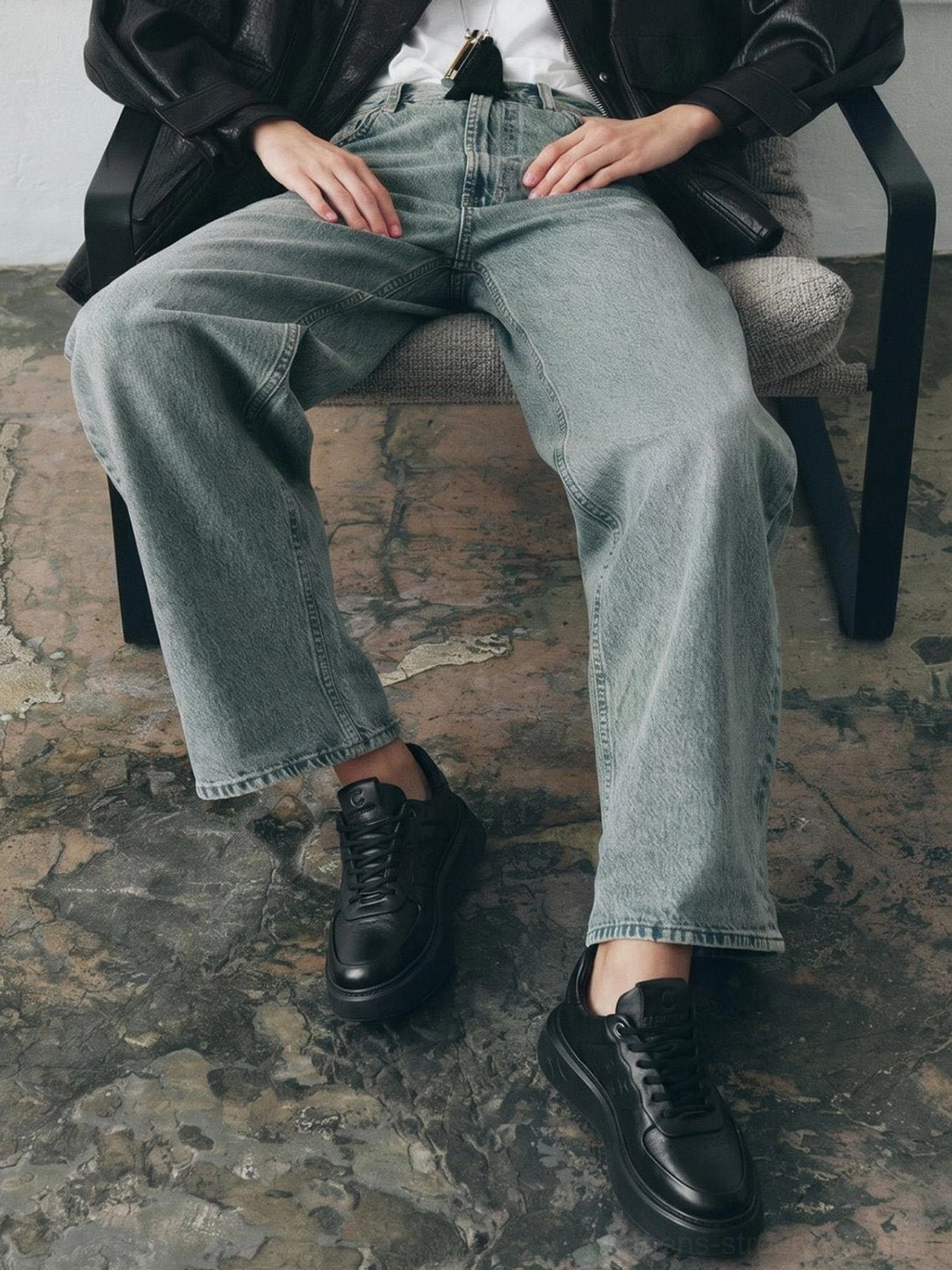 Black embossed low-top platform sneakers paired with wide-leg jeans in a relaxed contemporary streetwear look