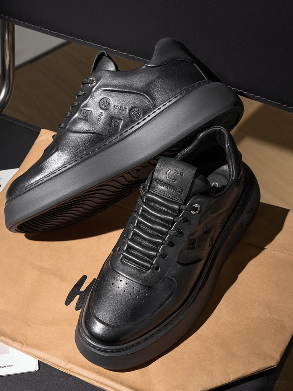 Pair of black embossed platform sneakers displayed on kraft paper showing perforated toe caps, laces, and thick soles
