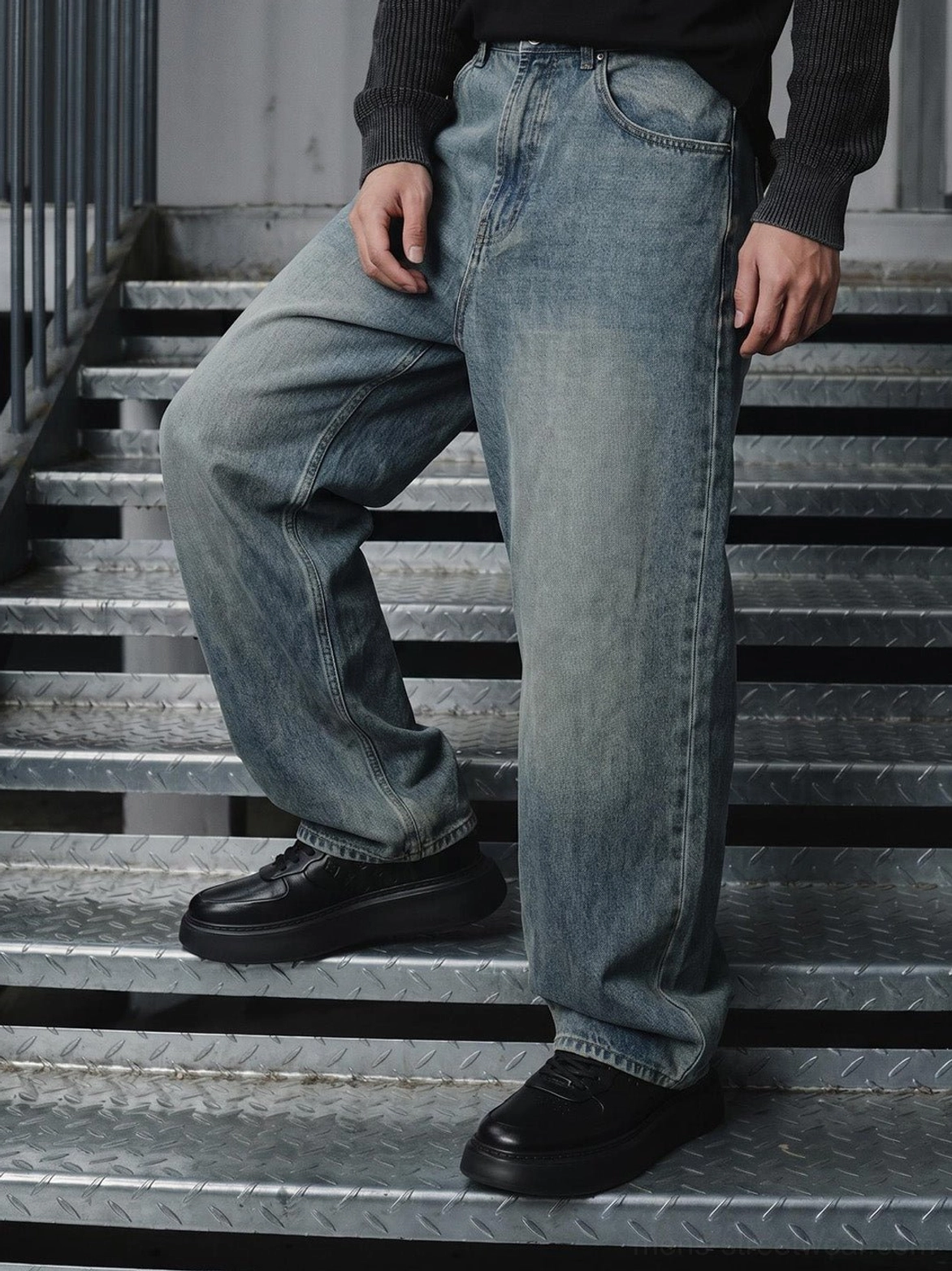 Rear side view of black platform sneakers worn with loose denim trousers in a modern urban outfit