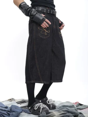 Side rear view of black embroidered denim culotte shorts with golden contrast stitching, back pocket embroidery, studded belt and platform streetwear styling