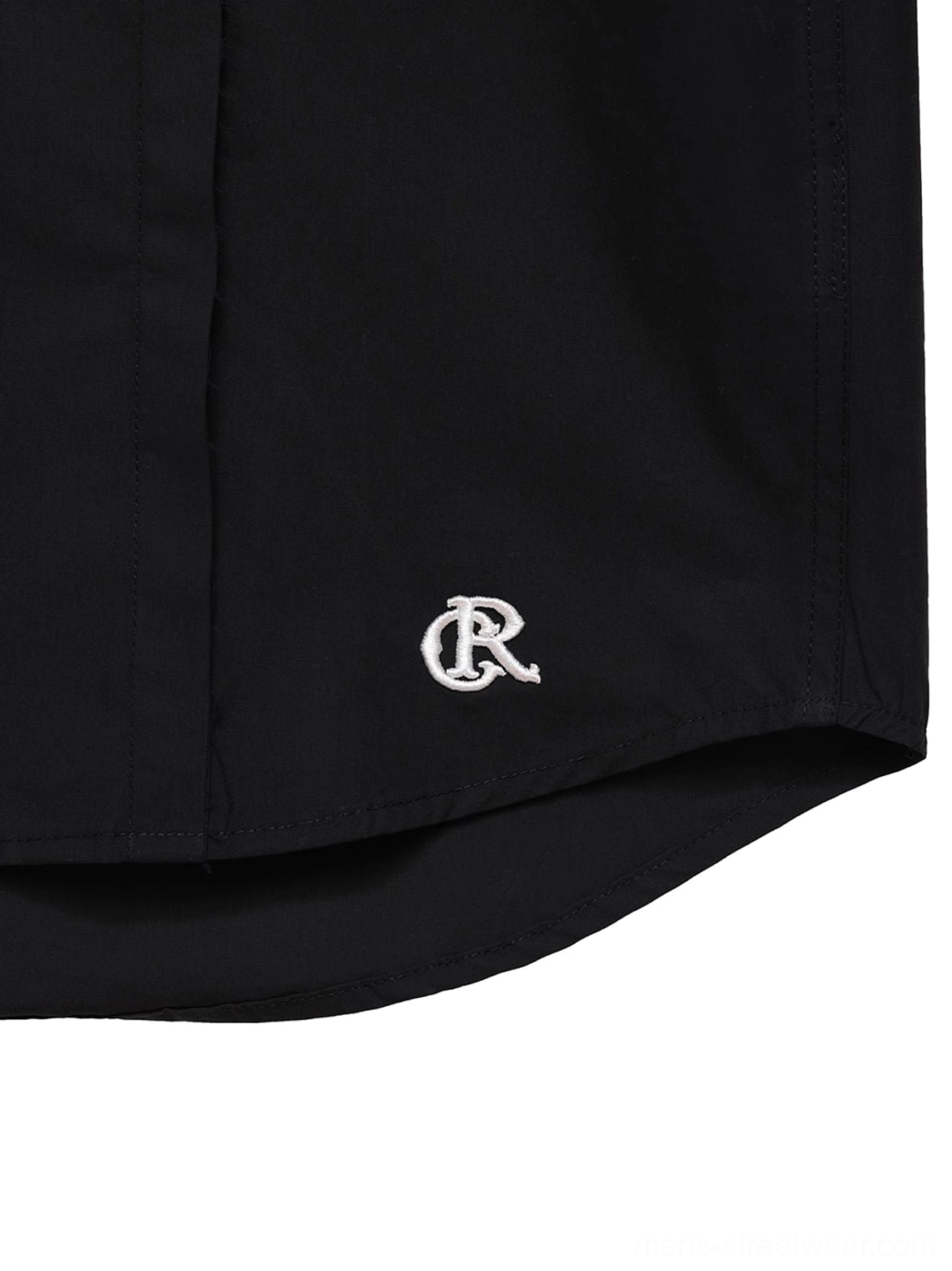 Close up of subtle white embroidered hem detail and precise side stitching on black cotton poplin streetwear shirt