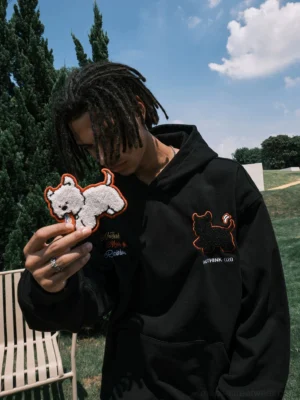 Black embroidered puppy graphic oversized pullover hoodie worn by male model outdoors in a grassy park