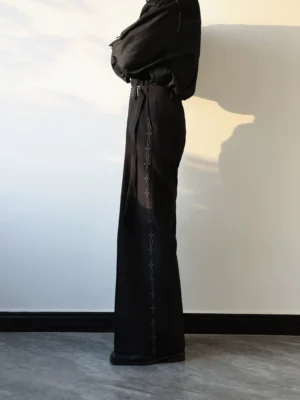 Black embroidered side seam wide-leg tailored pants shown in a full side profile with chain-style outer seam embroidery and leather shoes