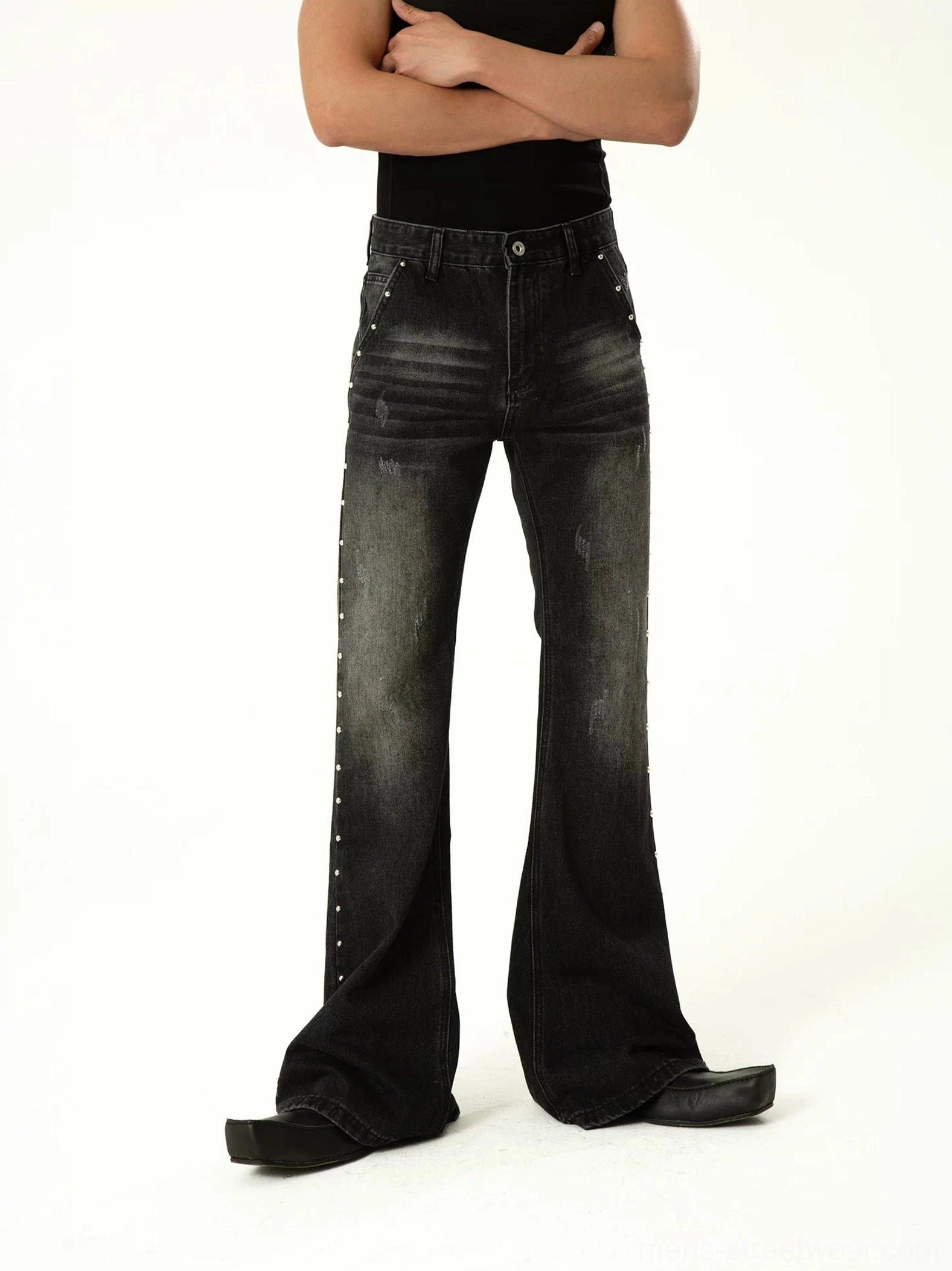 Front full-body view of faded black studded flare jeans featuring high-rise fit, outer side rivets, and dramatic bell-bottom legs