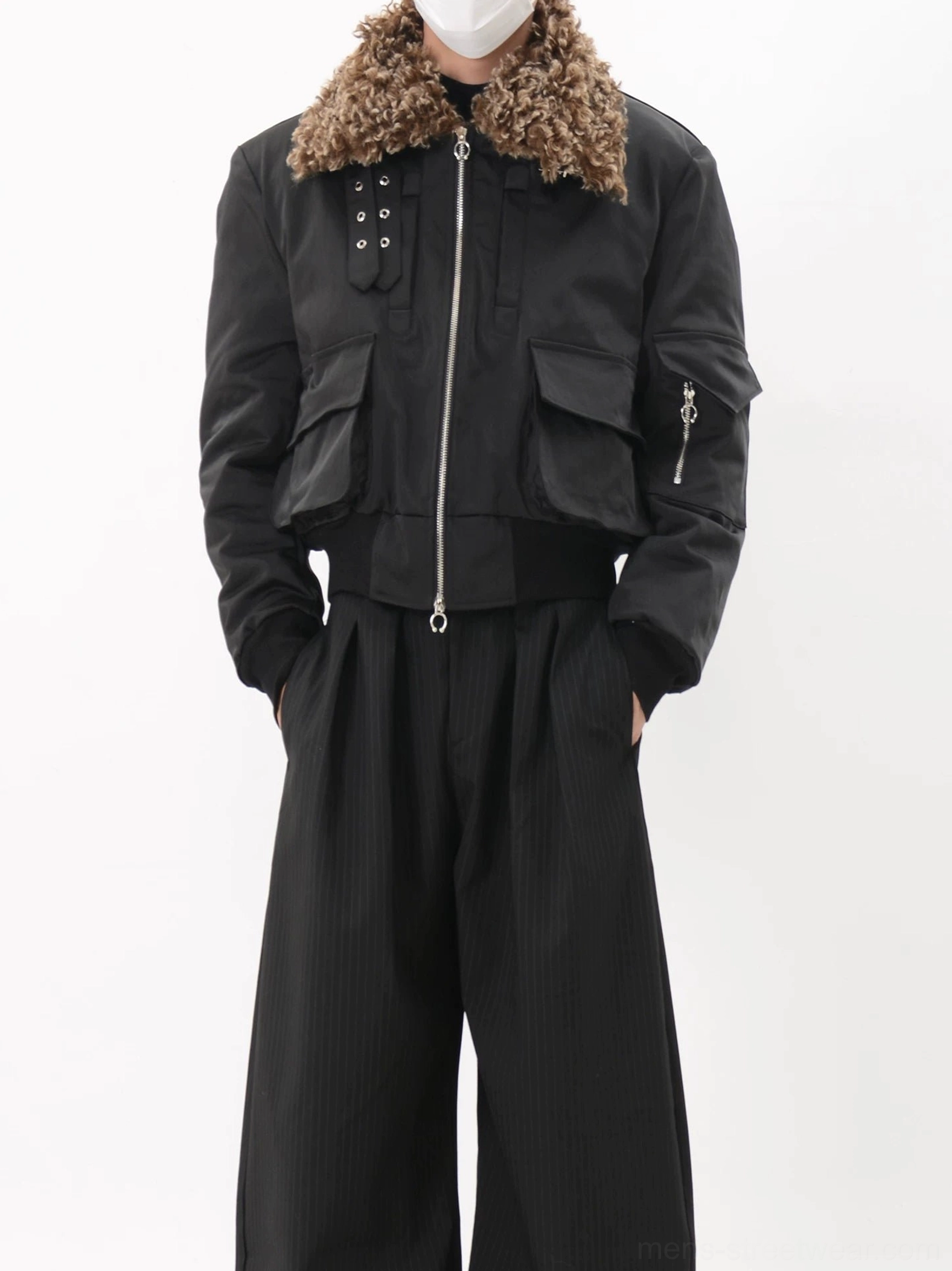 Close-up front view of black faux fur collar bomber jacket with curly brown collar, silver metal zipper, flap utility pockets and snap placket accents