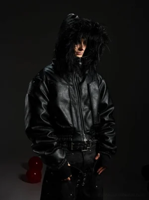 Front three-quarter view of a black faux leather hooded bomber jacket with oversized shaggy faux fur trim, cropped streetwear fit, front zipper, and elasticated waist