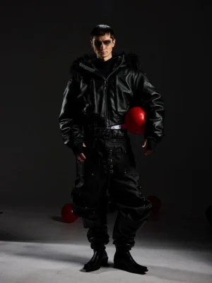 Full-body view of a black faux fur hooded leather bomber jacket styled with black cargo pants and boots, featuring a cropped silhouette and statement fur trim