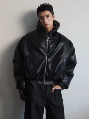 Close-up front view of black faux leather bomber jacket showing brown faux fur stand collar, metal zipper, elastic cuffs, and hem