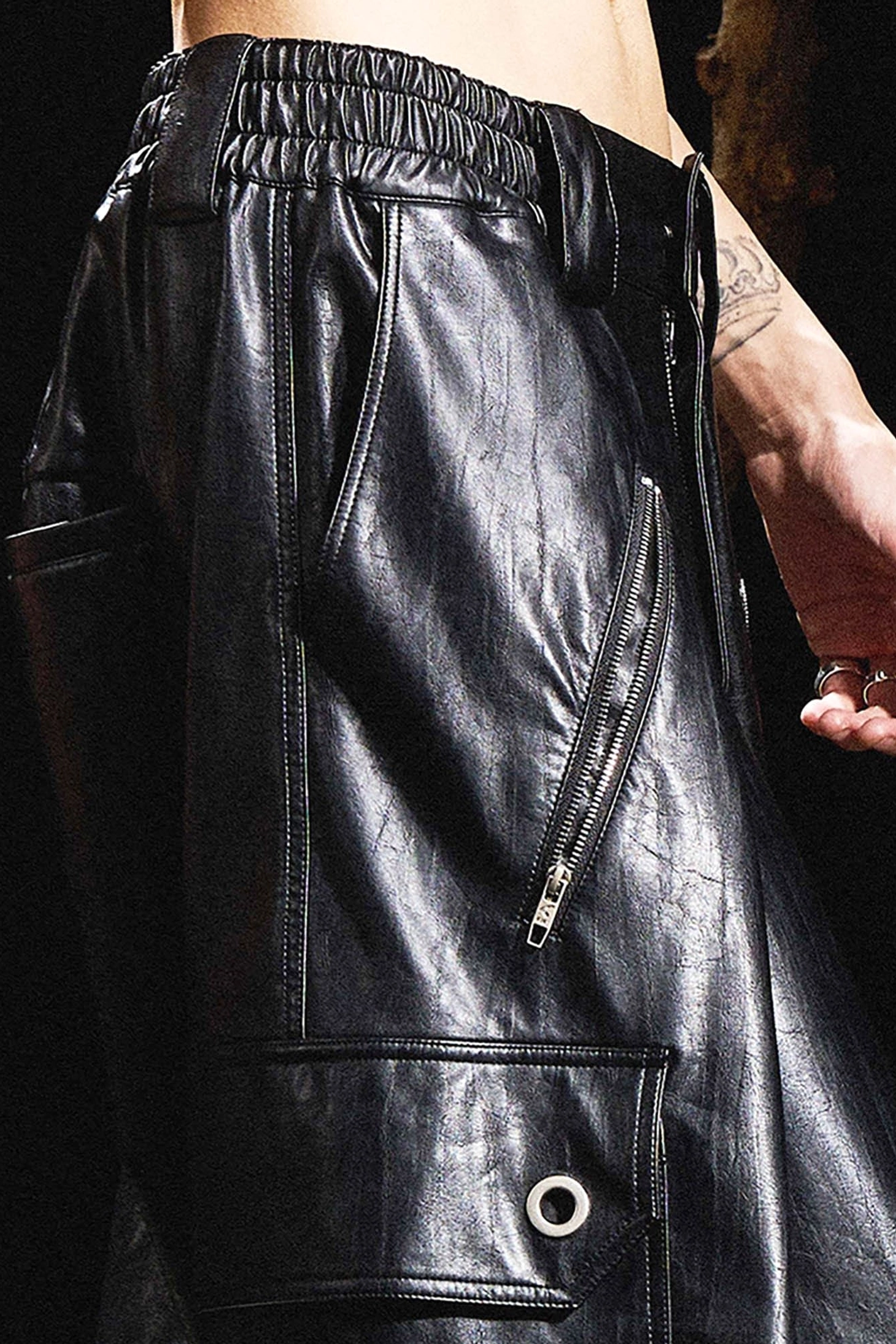 Close-up of black faux leather cargo pants waistband and upper thigh with elastic waist and zippered side pocket