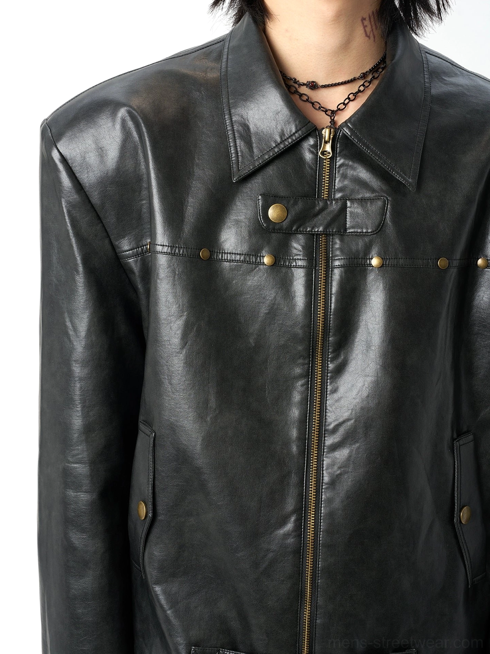 Close-up detail of black faux leather moto jacket chest and collar showing notch lapel, bronze center zipper, decorative studs, and vintage textured finish