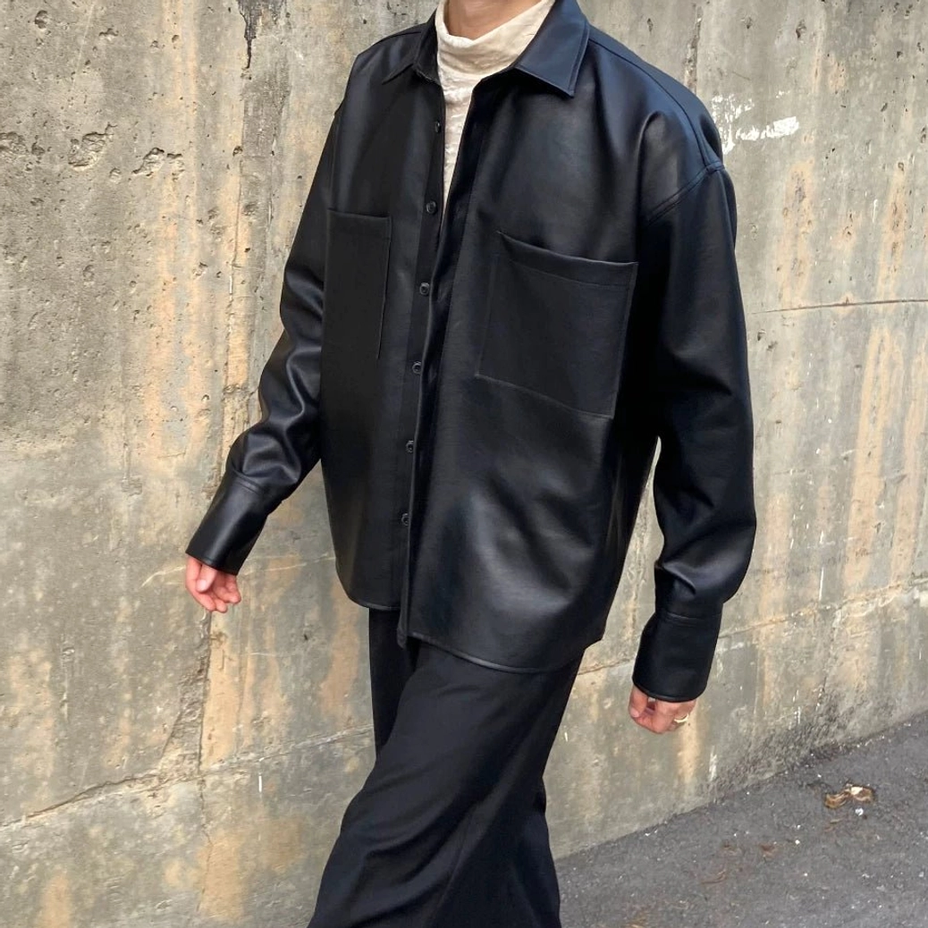 Front three quarter view of black faux leather shirt jacket with classic collar, two large chest pockets and dropped shoulder cut