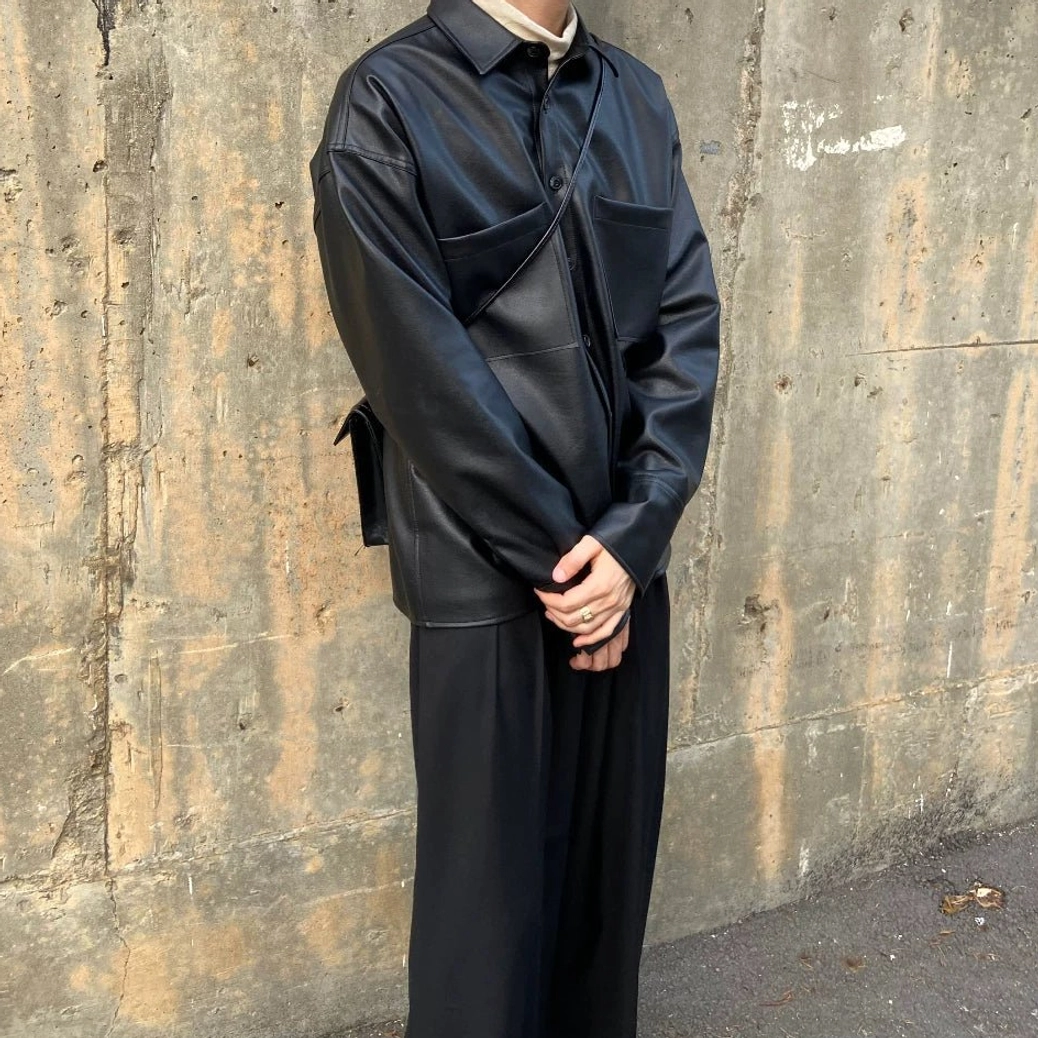 Side profile of black faux leather shirt jacket showing smooth PU leather fabric, relaxed fit and dual chest flap pockets