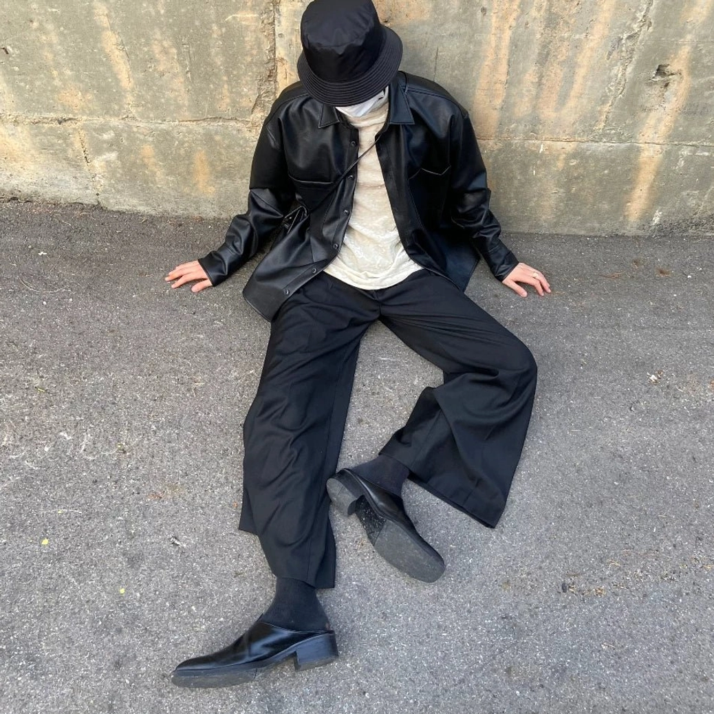 Seated styling view of unbuttoned black faux leather shirt jacket layered over a cream turtleneck with wide leg trousers