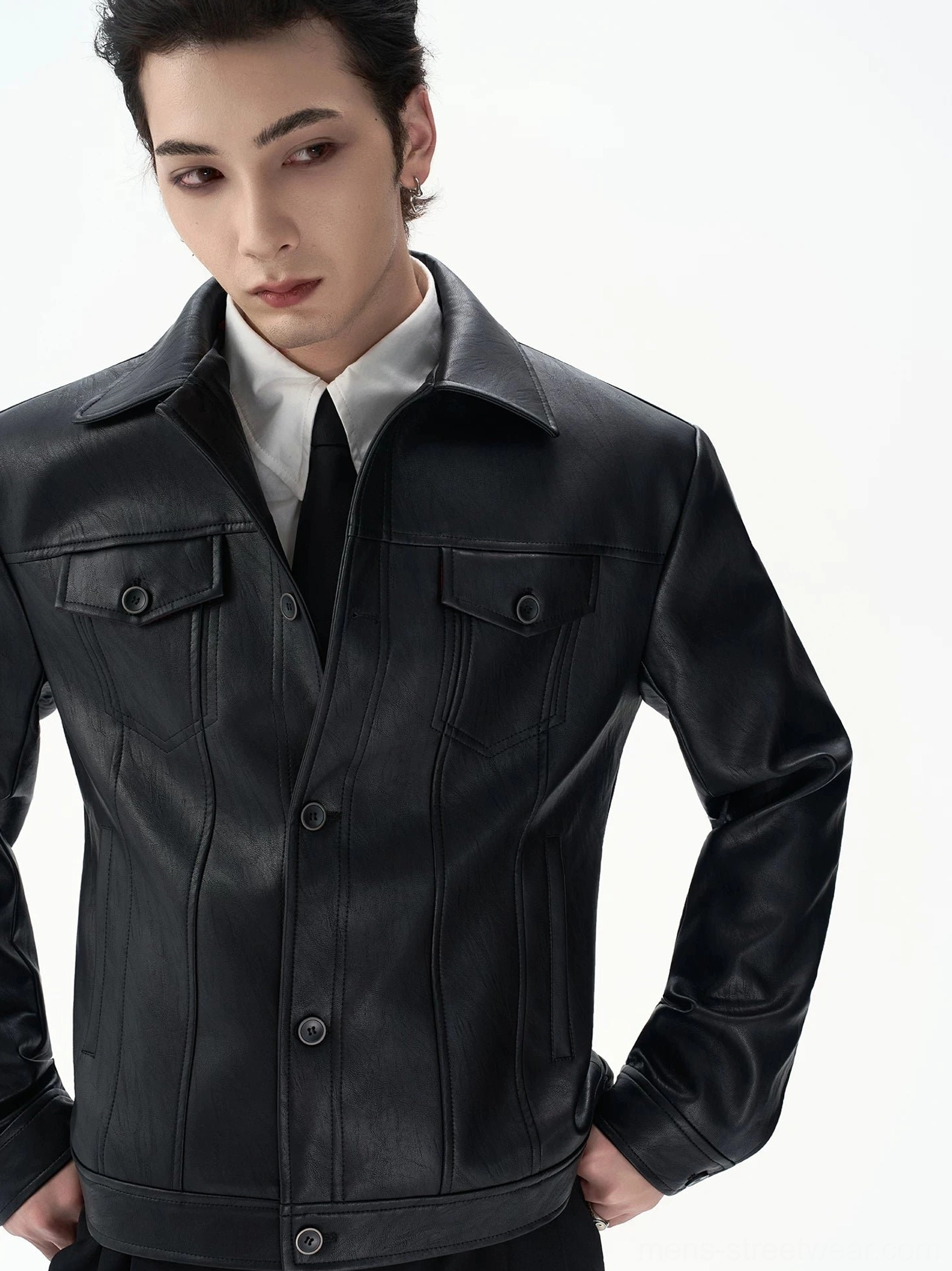 Male model wearing a black faux leather streetwear jacket over a white shirt and black tie showing structured shoulders chest flap pockets and detailed stitching