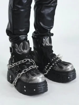 Low angle view of black and silver flame chain spike platform ankle boots styled with black faux leather trousers and chunky lug soles