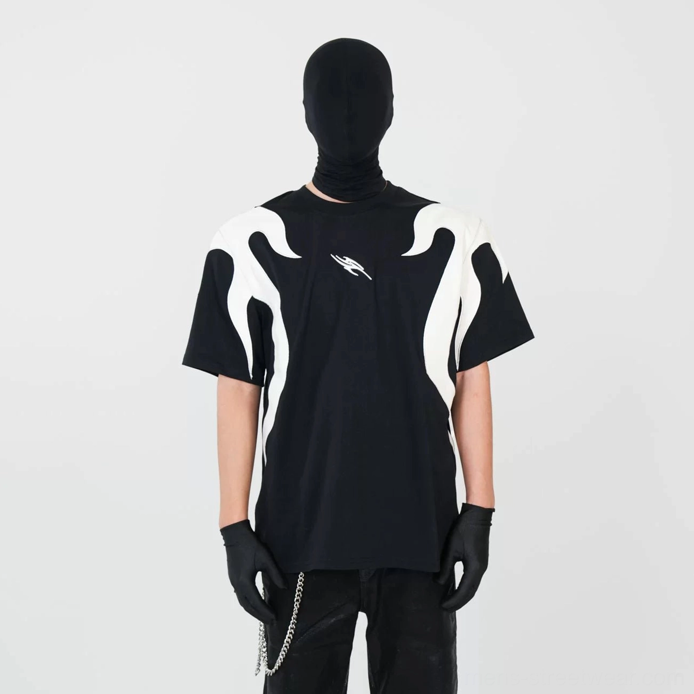 Direct front view of an oversized black flame panel T-shirt featuring a small chest emblem, bold off-white flame details, chain-decorated leather pants, and Y2K streetwear attitude