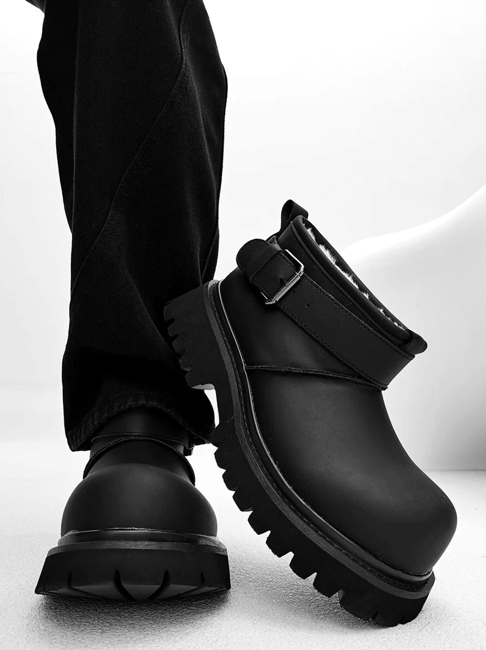 Black fleece-lined streetwear ankle boots shown from the rear with a thick sculpted rubber platform sole and buckle strap
