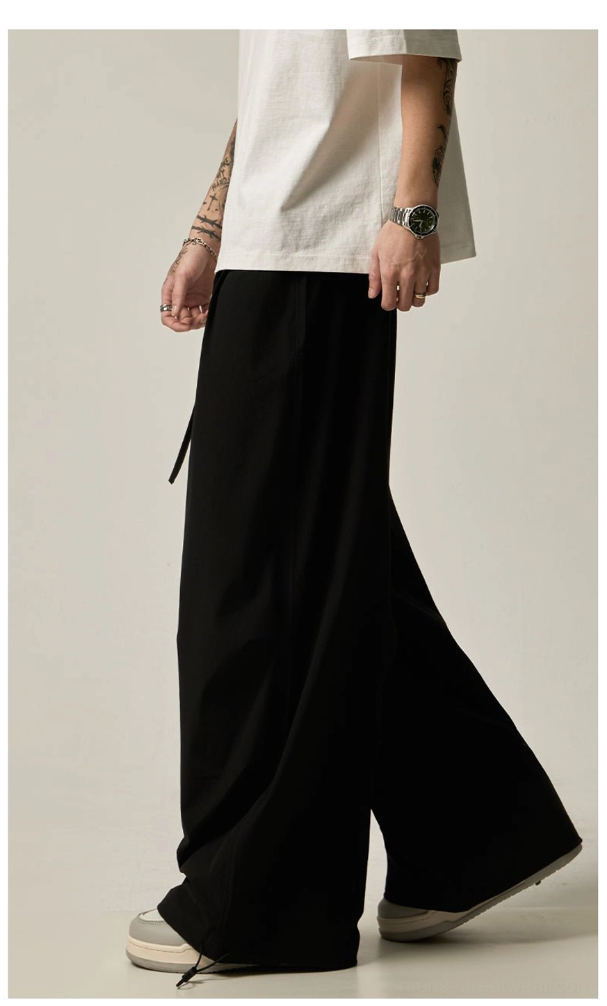 Black flowy wide leg streetwear pants for men shown from the side with a streamlined draped silhouette