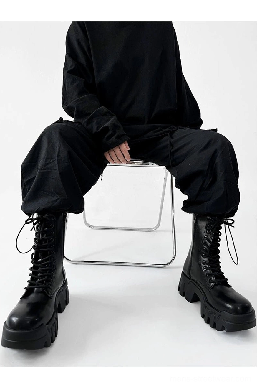 Black futuristic platform combat boots worn with all black streetwear outfit while seated on metal chair