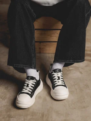 Black and white platform sneakers styled with dark wide-leg jeans and white crew socks in a modern streetwear outfit