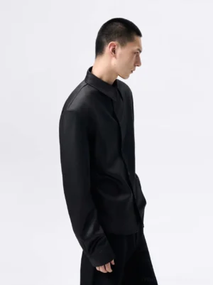Side view of black glossy cropped button-up shirt with structured shoulders, pointed collar, and tailored streetwear silhouette