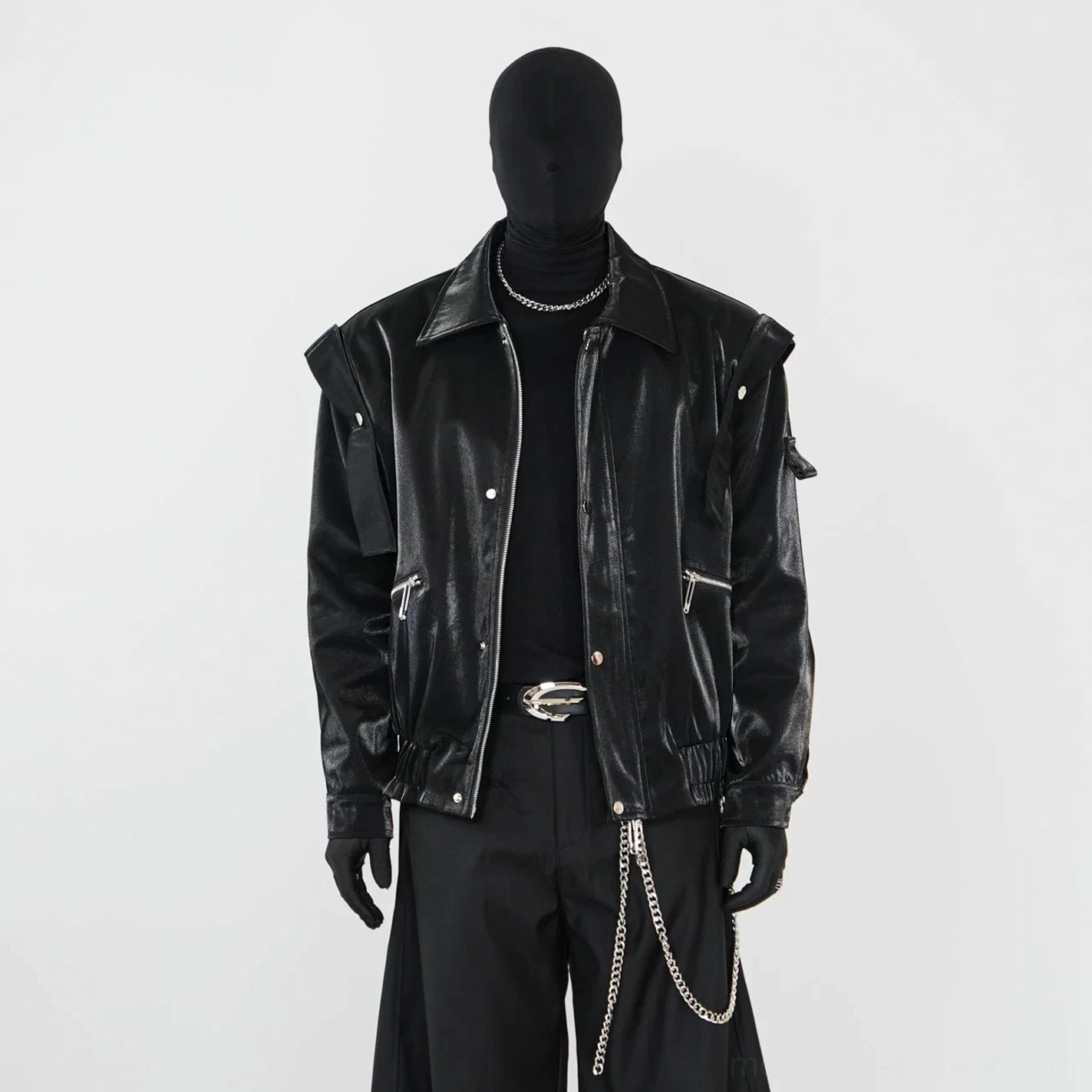 Close-up front view of black glossy biker jacket with metal snap placket, side zipper pockets, detachable shoulder patches, and belt buckle details