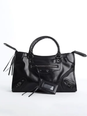Black glossy studded moto satchel bag in front three quarter view with front zipper pocket, patent faux leather finish, metal hardware, hanging tag and tassel pulls