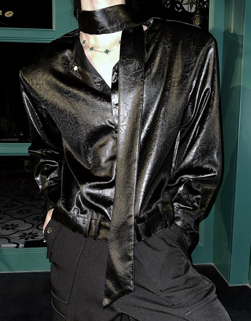 Close-up of black glossy tie-neck shirt collar, deep V neckline, matching tie, and reflective fabric texture