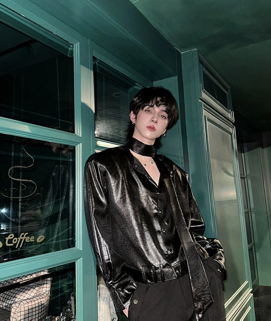 Side view of black glossy tie-neck shirt styled with cargo trousers and layered streetwear accessories