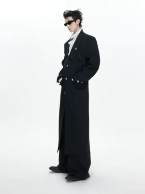 Side profile of male model wearing oversized black gothic double-lapel floor-length trench coat in white studio