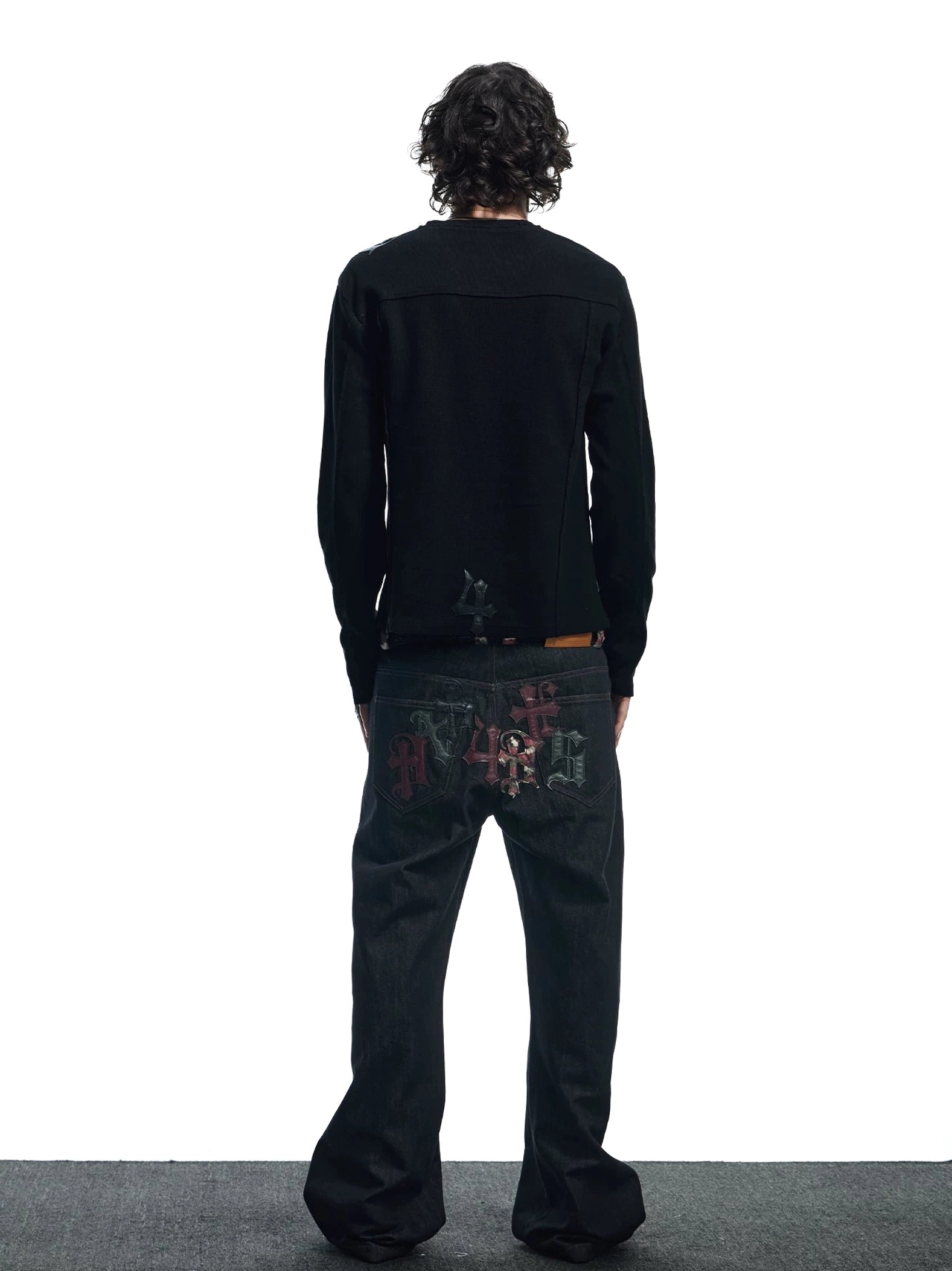 Back view of male model wearing black Gothic letter appliqué straight-leg jeans with decorated back pockets