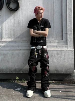 Male model wearing black Gothic letter appliqué straight-leg denim jeans with a graphic T-shirt and white platform shoes outdoors