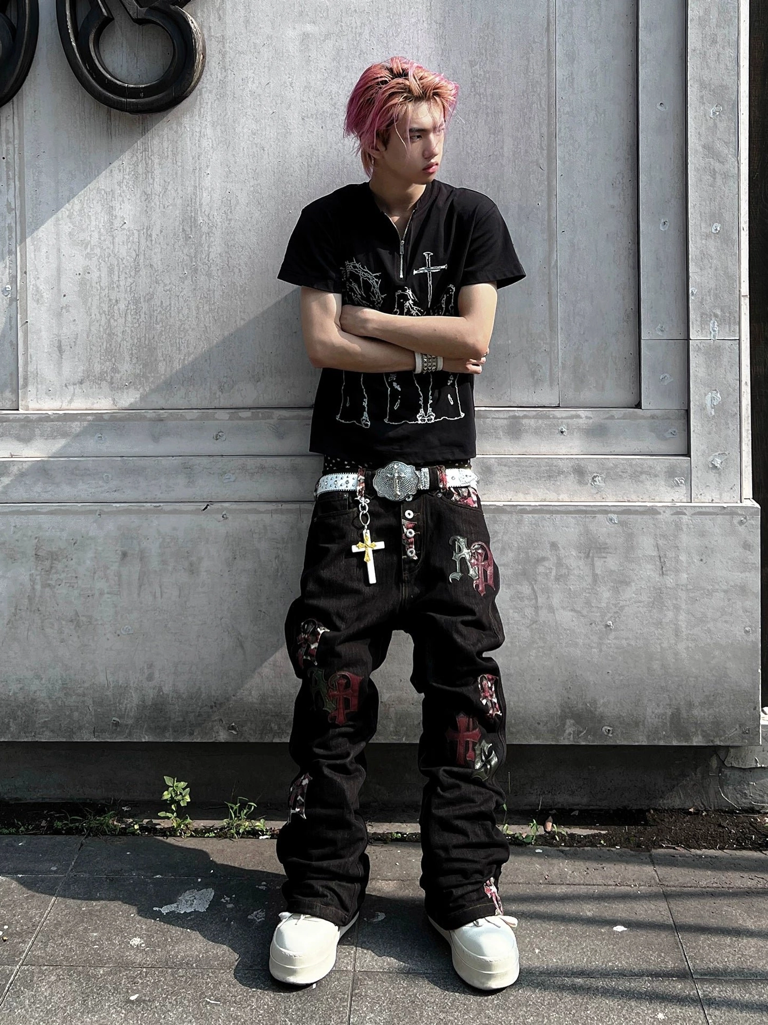 Male model wearing black Gothic letter appliqué straight-leg denim jeans with a graphic T-shirt and white platform shoes outdoors