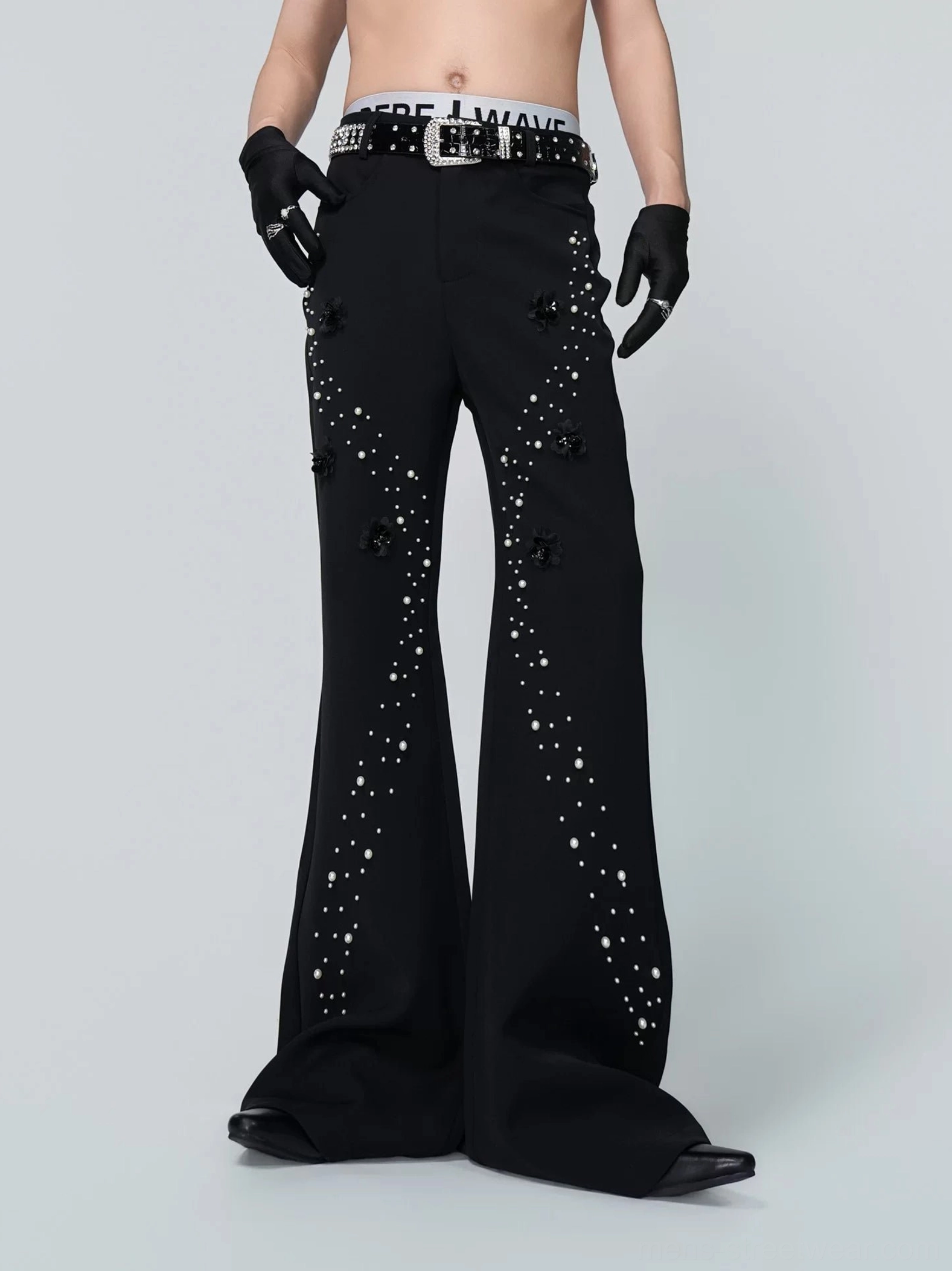Front full-body view of black gothic embellished flare trousers with 3D floral appliques, pearl-style star details, dramatic wide legs, and matching studded belt