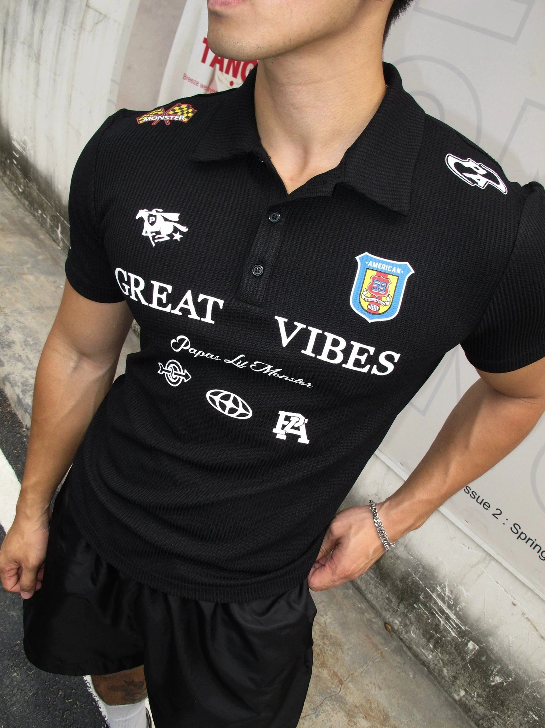 Black Great Vibes graphic ribbed polo shirt shown in a close front view with structured collar button placket varsity badges and football-inspired streetwear graphics