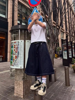 Black and green shell-toe platform streetwear sneakers worn with a white t-shirt and navy wide-leg trousers on a downtown city street