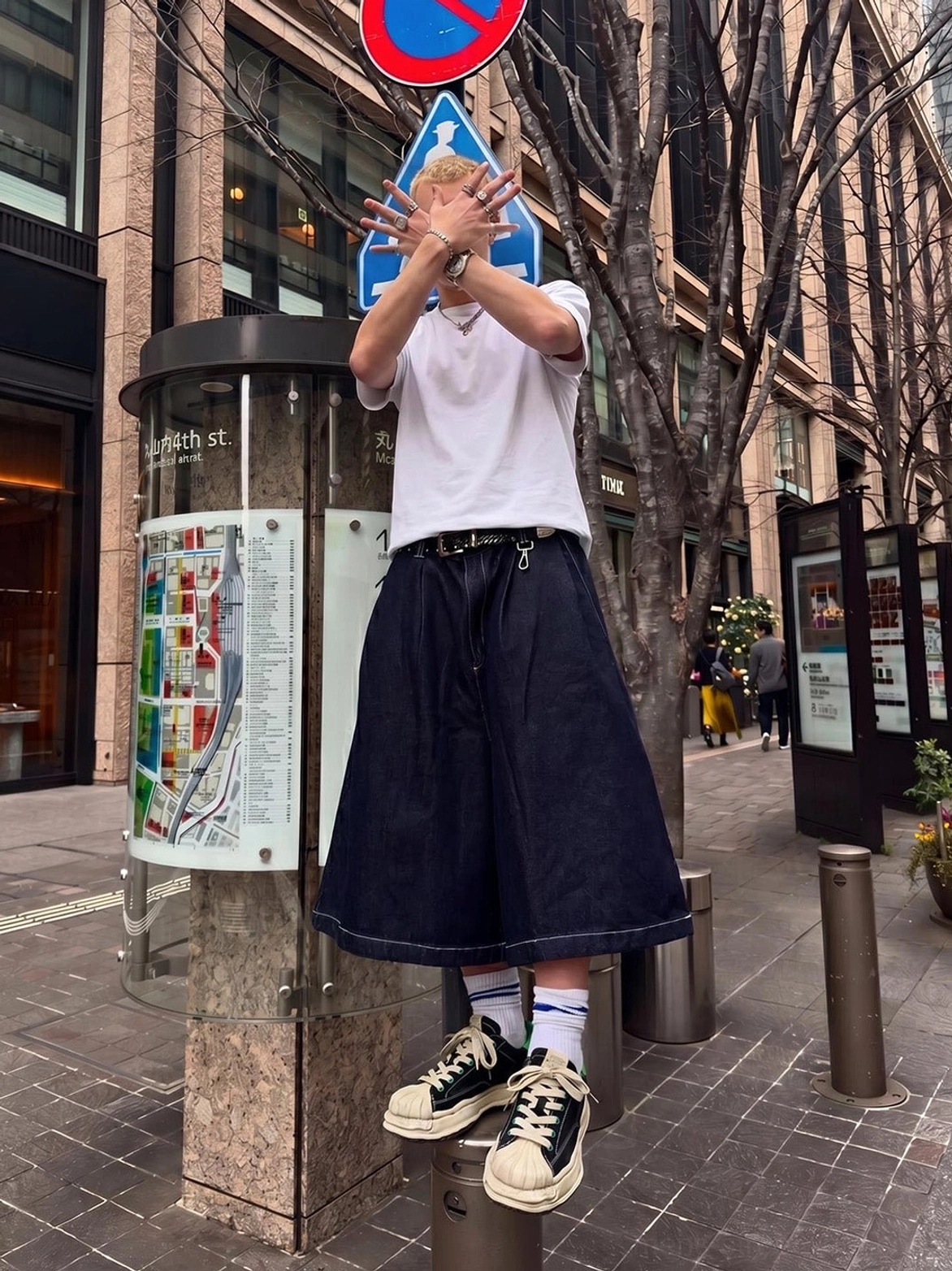 Black and green shell-toe platform streetwear sneakers worn with a white t-shirt and navy wide-leg trousers on a downtown city street