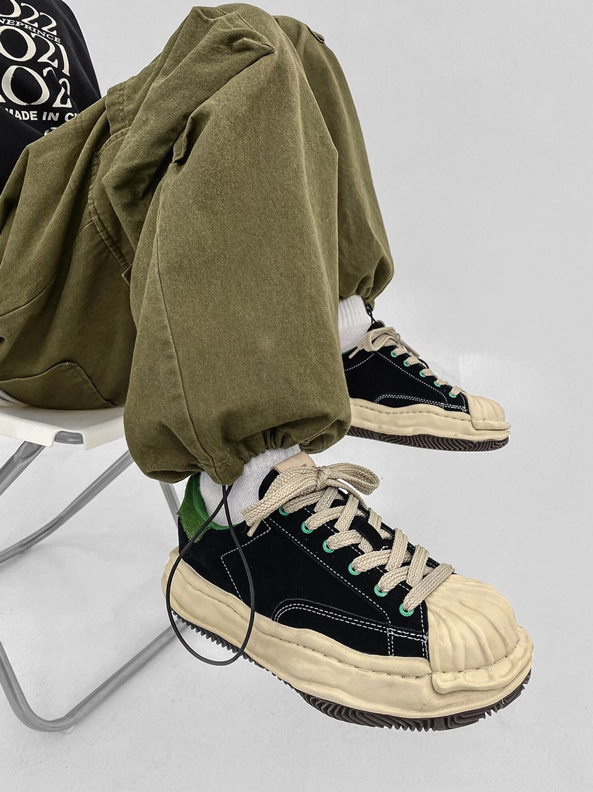 Black and green platform shell-toe sneakers paired with olive cargo pants, showing the cream sole, green lining, and lace-up design