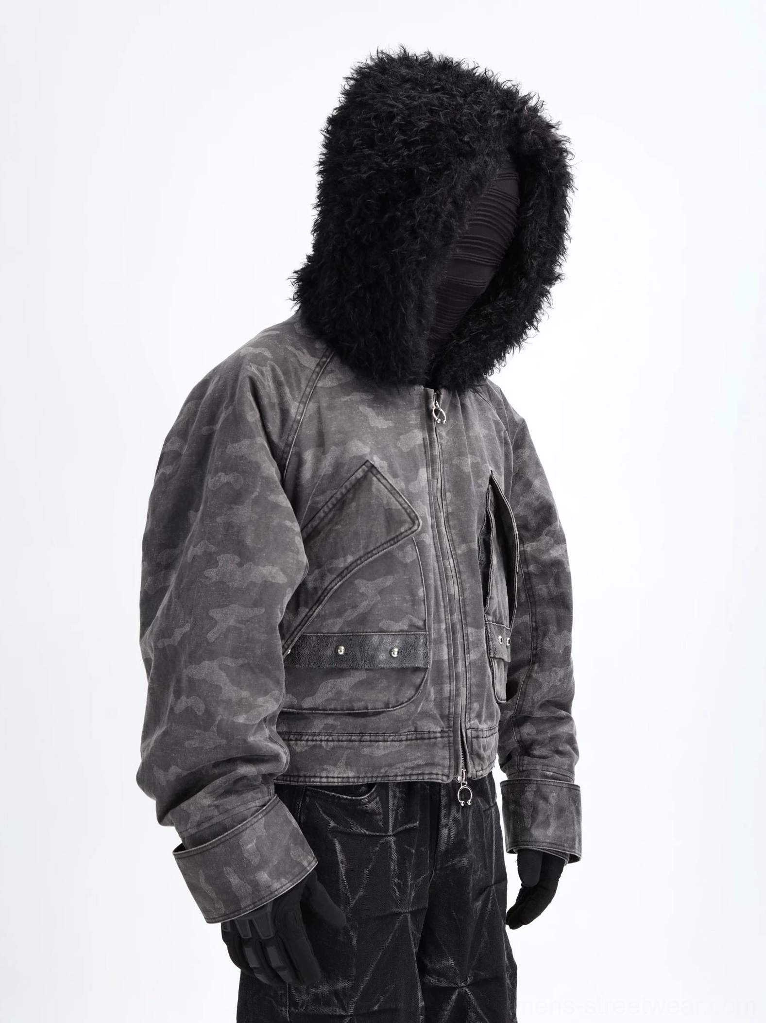 Black and grey camo faux shearling hooded cropped bomber jacket shown on a mannequin with black curly hood trim, oversized utility pockets, metal hardware, and waxed black trousers
